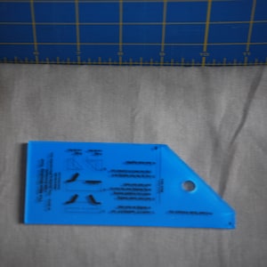 May include: A blue plastic sewing tool with a hole in the corner and instructions printed on the surface. The tool is used for marking fabric.