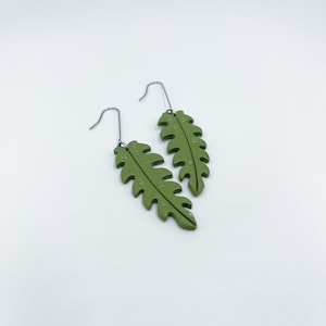 May include: A pair of green leaf-shaped earrings with silver hooks. The leaves have a textured surface and are slightly curved.