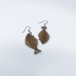 May include: A pair of brown fish-shaped earrings with silver hooks. The fish have a detailed design with black dots and lines.