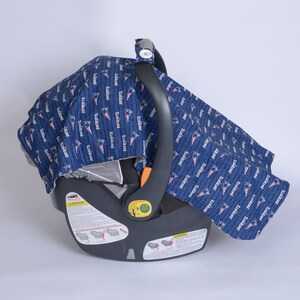 May include: A blue and white baby car seat cover with the word "Patriots" repeated throughout the fabric. The cover is on a black car seat with a warning label.