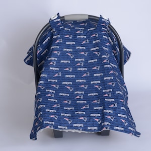 May include: A blue and white car seat cover with a repeating pattern of the New England Patriots logo and the word "Patriots".