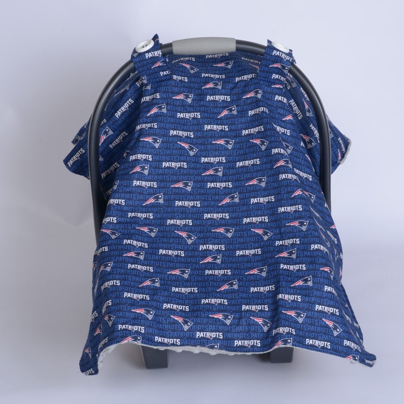 May include: A blue and white car seat cover with a repeating pattern of the New England Patriots logo and the word "Patriots".