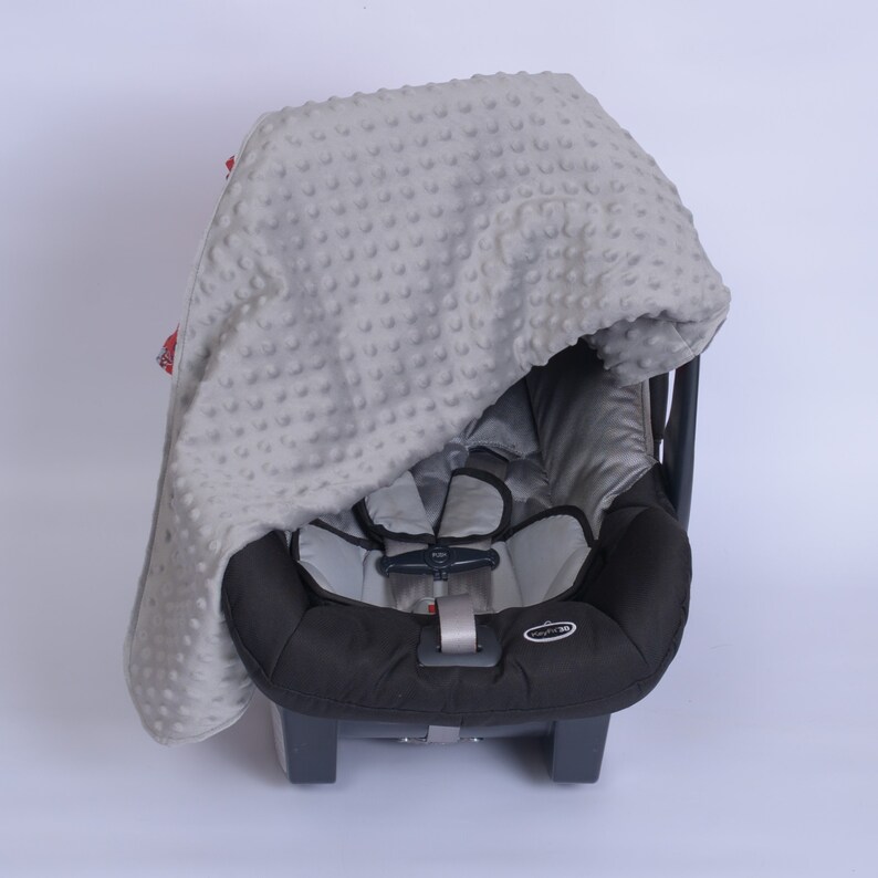 May include: A grey and white baby car seat cover with a grey and white polka dot pattern. The cover is made of soft, breathable fabric and is designed to protect the car seat from spills and stains.