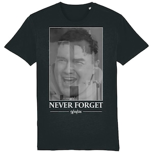 Puede incluir: Camiseta negra con una imagen en escala de grises de la cara de un hombre superpuesta a un paisaje urbano. El texto "NEVER FORGET - 9/11/01" está impreso debajo de la imagen.