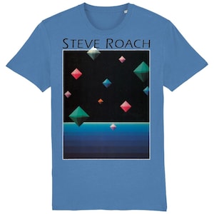 May include: A light blue t-shirt featuring a graphic of a black background with colourful geometric shapes and the text "STEVE ROACH" printed on the front.