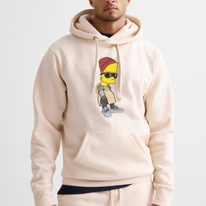 May include: A cream-colored hoodie with a cartoon character wearing sunglasses and a red beanie. The character is yellow and has a blue outline. The hoodie has a kangaroo pocket and a drawstring hood.