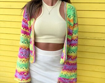 May include: A colorful striped crochet cardigan with bell sleeves. The cardigan is made with a variety of bright colors, including pink, yellow, green, and purple. The cardigan is open in the front and has a relaxed fit.