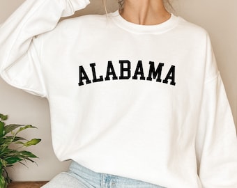 Puede incluir: Una sudadera blanca con la palabra "ALABAMA" impresa en negro, en una fuente universitaria. La sudadera la lleva puesta una persona. La imagen está etiquetada como "ARCHIVO DIGITAL PNG | SVG".