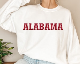 Puede incluir: Sudadera blanca con la palabra "ALABAMA" en letras de bloque granate en el pecho. La sudadera tiene cuello redondo y mangas largas. La parte inferior de la imagen tiene el texto "DIGITAL FILE PNG | SVG".