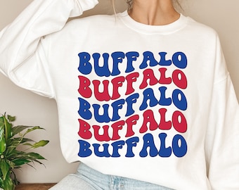 May include: White sweatshirt with the word "BUFFALO" repeated in a grid pattern. The word is in a retro font, alternating between red and blue. The bottom of the image reads "DIGITAL FILE PNG | SVG".