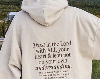 May include: A beige hoodie with a hood and long sleeves. The back of the hoodie features the text "Trust in the Lord with ALL your heart & lean not on your own understanding; In all your ways submit to Him, and He will make your paths straight. Proverbs 3:5-6."
