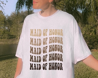 May include: White oversized t-shirt with the text "Maid of Honor" repeated five times in a brown and gold gradient font.