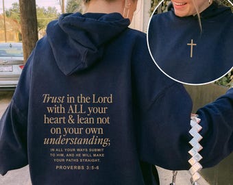 May include: Navy blue hoodie with the text "Trust in the Lord with ALL your heart & lean not on your own understanding;" on the back. A small gold cross is on the front. The hoodie is paired with light blue jeans.