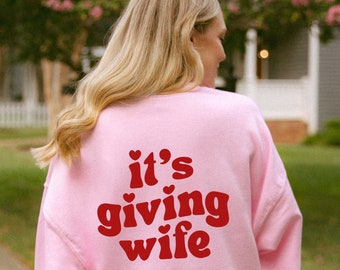 May include: Pink sweatshirt with the text "it's giving wife" in red retro font with hearts.