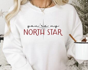 May include: White sweatshirt with the text "you're my NORTH STAR" in red and grey lettering. A grey star graphic is above the text.