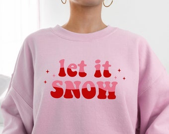 May include: Pink sweatshirt with a red and pink graphic that says "let it snow" in a retro font.