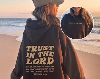 May include: A dark brown hoodie with the text "TRUST IN THE LORD" in a cream-colored, retro font on the back. The hoodie also features a quote from Proverbs 3:5-6. The front of the hoodie has the text "TRUST IN THE LORD".