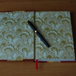May include: A closed book with a marbled cover in shades of green and white. A black pen is lying open on the book.