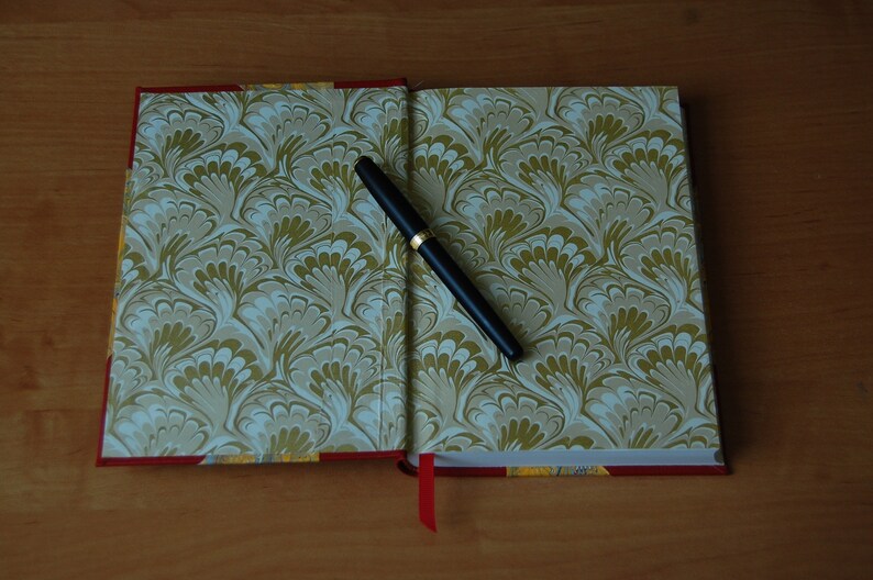 May include: A closed book with a marbled cover in shades of green and white. A black pen is lying open on the book.