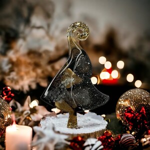 May include: A black and gold resin Christmas tree ornament with a swirl design. The ornament is sitting on a white base with a wood texture.