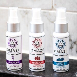 May include: Three small white bottles with silver caps and labels. The labels are white with a blue, red, or purple circle and text that reads "OMAZE - MIST N' GO - TOILET FRESHENER". The bottles are labeled with the scents "Lavender", "Blossom", and "Dream".