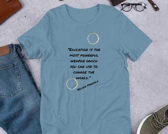 Pode incluir: Uma camiseta azul claro com uma citação de Nelson Mandela sobre a educação como a arma mais poderosa. A citação está impressa em texto preto com dois anéis de xícara de café em dourado.