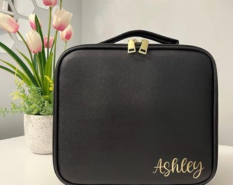 Könnte beinhalten: Schwarze Reißverschluss-Kosmetiktasche für Reisen mit goldenen Beschlägen und dem Namen "Ashley" in goldener Schrift auf der Vorderseite.