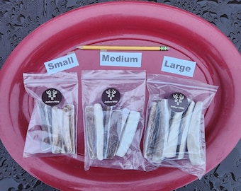 May include: Three clear plastic bags containing antler chews, labeled "Small," "Medium," and "Large." Each bag has a circular sticker with a deer antler logo and the text "Antlers Wild." A yellow pencil is placed across the top for size comparison. The chews are various shades of brown and white.