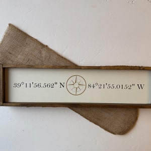 May include: A wooden sign with a compass and the coordinates 39°11'56.562" N 84°21'55.0152" W.