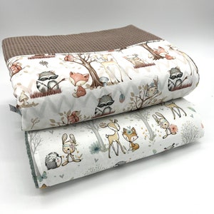 Könnte beinhalten: Zwei Babydecken mit Waldtiermotiven. Die obere Decke hat einen braunen Waffelrand und einen weißen Hintergrund mit Illustrationen von Waschbären, Füchsen und Hirschen. Die untere Decke hat ein ähnliches Design mit Kaninchen und Igeln.