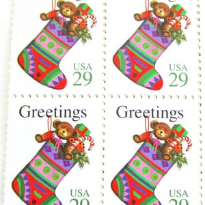 May include: Sheet of four "Greetings" postage stamps. Each stamp features a Christmas stocking design with a teddy bear, candy canes, and a gift. The stamps are marked "USA 29". The stocking is red, green, purple, and pink.