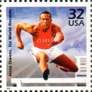 May include: A red, white, and blue postage stamp featuring a black and white image of Jesse Owens, an American track and field athlete, in mid-jump over a hurdle. The stamp reads "Jesse Owens, Six World Records" and "32 USA".