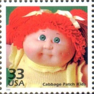 May include: A postage stamp featuring a Cabbage Patch Kids doll. The doll has red yarn hair, green eyes, and rosy cheeks. The stamp reads "33 USA" and "Cabbage Patch Kids".