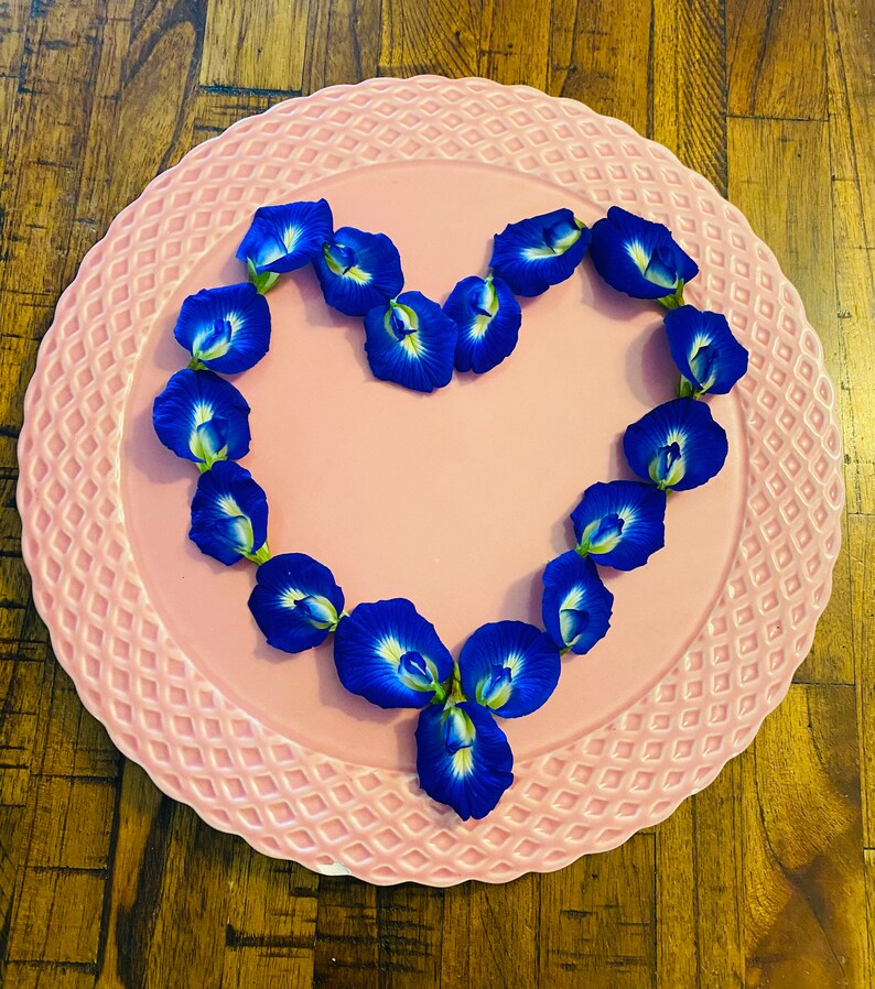 May include: A pink plate with a scalloped edge features a heart shape made of blue butterfly pea flowers.