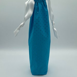 May include: A tall, turquoise drawstring bag with a pattern of small, darker blue dots. The top of the bag is gathered and secured with a white satin ribbon that forms a handle. The bag is made of a soft fabric.