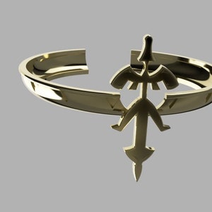 以下が含まれることがあります： オープンデザインのゴールドカラーのリング。リングは、中央の矢印の形と翼のような要素を持つ様式化されたエンブレムが特徴です。リングは灰色の背景に配置されています。