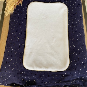 Peut inclure: Un tapis à langer bleu marine avec des pois dorés et un insert blanc en peluche. Le tapis a des liens aux coins et le nom "Adonis" est brodé en or sur le dessus.