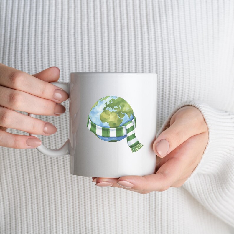 May include: White ceramic mug featuring a watercolor illustration of Earth wearing a green and white striped scarf. The mug is held by a person wearing a white sweater. The Earth illustration shows the continents in green and the oceans in blue.
