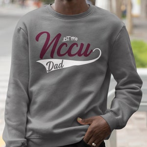 May include: Grey sweatshirt with a white and maroon graphic. The graphic says "NCCU EST. 1910" in a cursive font with a white baseball-style tail that says "Dad".