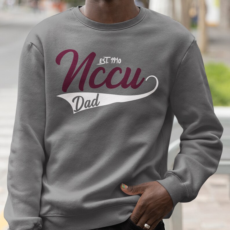 May include: Grey sweatshirt with a white and maroon graphic. The graphic says "NCCU EST. 1910" in a cursive font with a white baseball-style tail that says "Dad".
