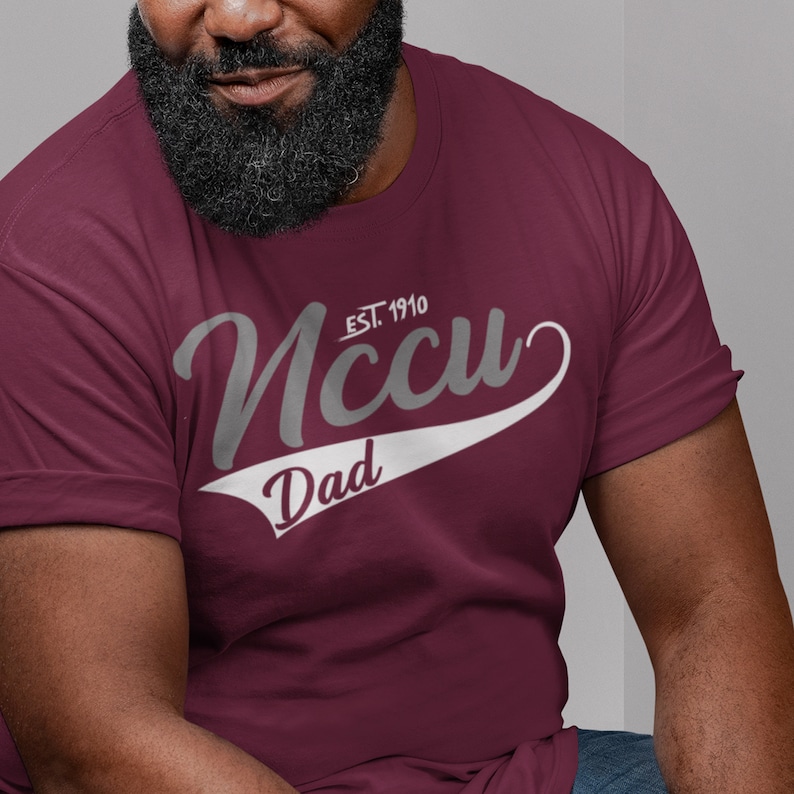 May include: Burgundy t-shirt with a white and grey graphic that says "NCCU EST. 1910" with a white baseball bat and the word "Dad" underneath.