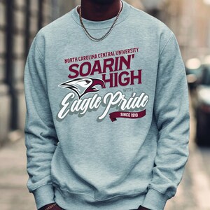 May include: A light gray sweatshirt with the text "North Carolina Central University" and "Soarin' High with Eagle Pride Since 1910". The sweatshirt features a maroon and white eagle logo.