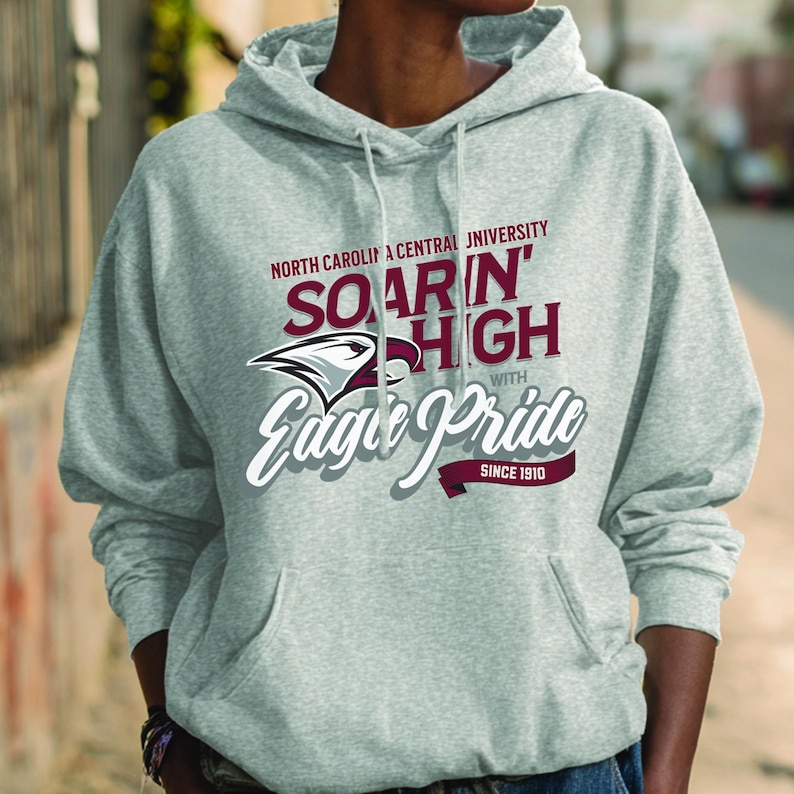 May include: A light gray hoodie with a front pocket and drawstring. The hoodie features the text "North Carolina Central University" and "Soarin' High with Eagle Pride Since 1910" in maroon and white. An eagle logo is also present.