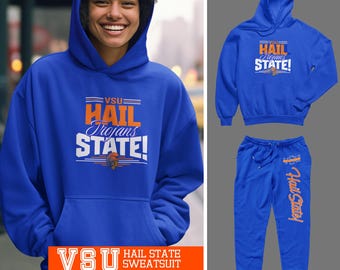 Può includere: Un completo tuta blu reale con felpa con cappuccio e pantaloni della tuta abbinati. La felpa con cappuccio e i pantaloni della tuta presentano la scritta "HAIL Trojans STATE!" in bianco e arancione. L'immagine mostra anche la scritta "VSU HAIL STATE SWEATSUIT".