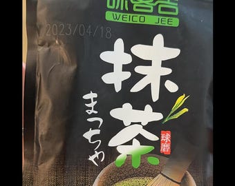 Puede incluir: Una bolsa negra con una etiqueta verde y blanca que dice "味客吉 WEICO JEE" y "抹茶 Matcha". La bolsa contiene 100 g de polvo de matcha y tiene una fecha de 2023/04/18 impresa.
