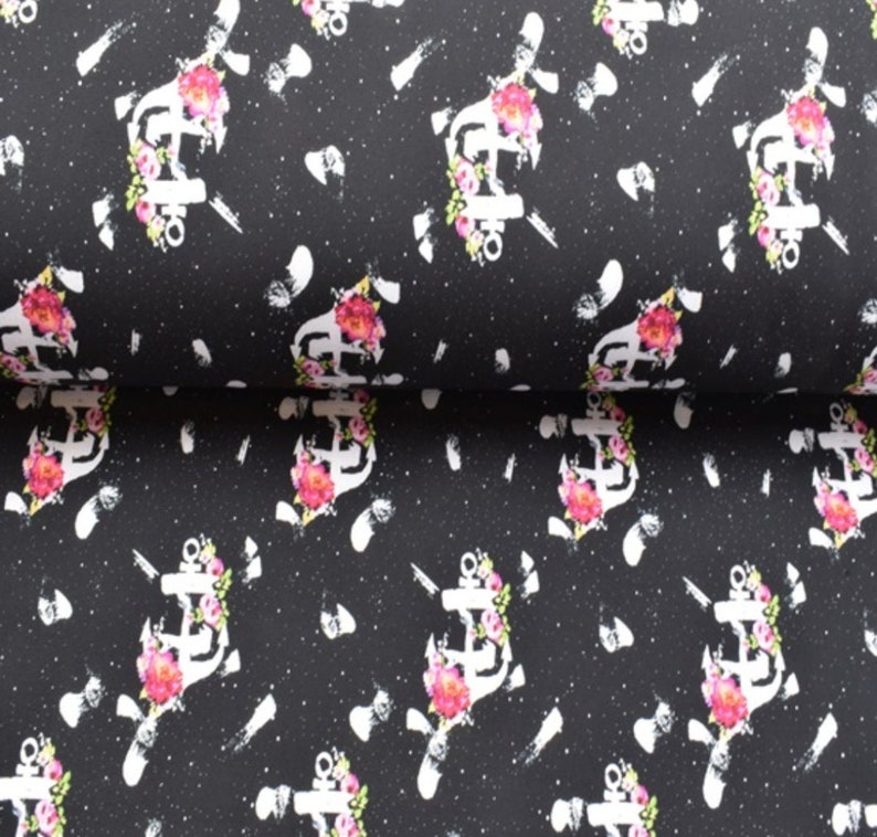 May include: Black fabric with a white anchor and pink flowers pattern. The anchor is surrounded by flowers and has a white outline. The background is black with white speckles.