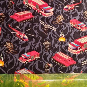 May include: Red and black fabric with a repeating pattern of fire trucks, helicopters, and firefighters. The fabric has a dark blue background with a flame-like design.