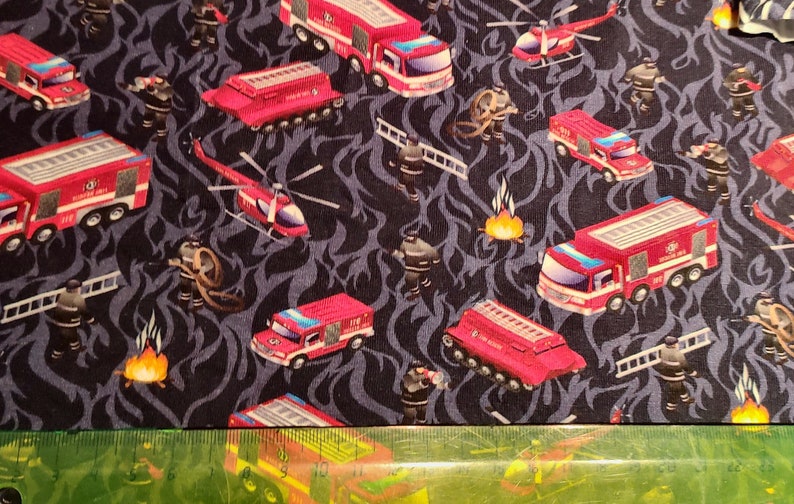 May include: Red and black fabric with a repeating pattern of fire trucks, helicopters, and firefighters. The fabric has a dark blue background with a flame-like design.