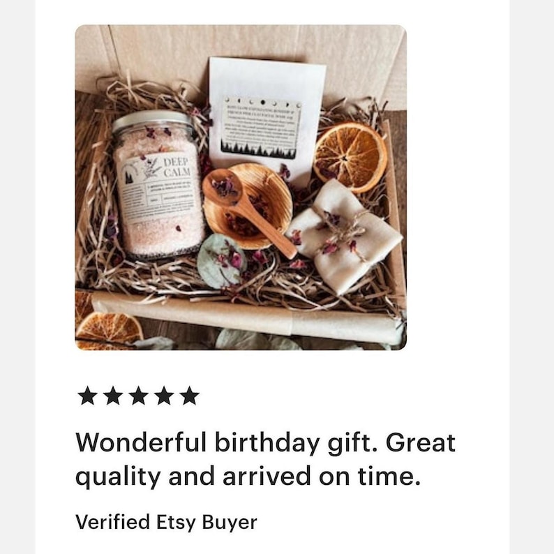 K&ouml;nnte beinhalten: Eine Geschenkbox gef&uuml;llt mit Papierstreifen, die ein Glas mit rosa Badesalz mit der Aufschrift Deep Calm, einen wei&szlig;en Beutel, eine kleine Holzschale mit Holzl&ouml;ffel, eine getrocknete Orangenscheibe und ein mit Schnur und Bl&uuml;tenbl&auml;ttern gebundenes Tuch enth&auml;lt.