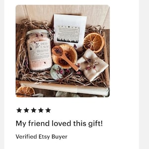 K&ouml;nnte beinhalten: Eine Geschenkbox gef&uuml;llt mit Holzsp&auml;nen, die ein Glas mit rosa Badesalz mit der Aufschrift Deep Calm, einen wei&szlig;en Beutel, eine kleine Holzschale mit Holzl&ouml;ffel, eine getrocknete Orangenscheibe und ein mit Bindfaden umwickeltes St&uuml;ck Seife enth&auml;lt.
